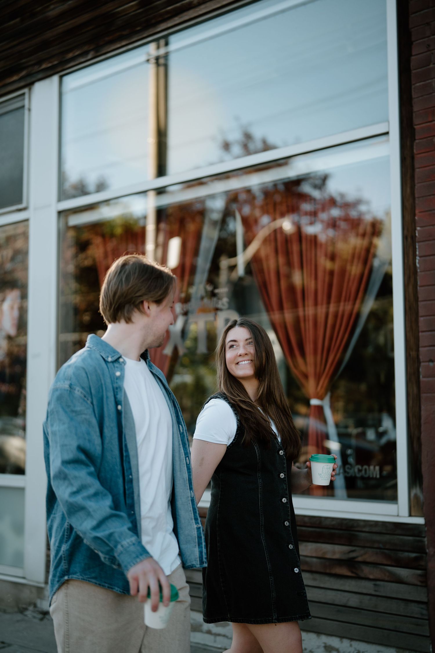 A couple shares a romantic moment outside a storefront window with a rake display during sunset.