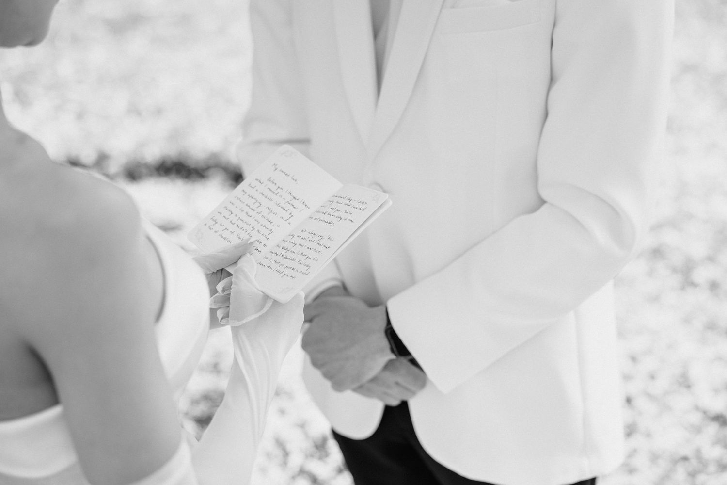 A person in a white shirt holds an open book during an outdoor ceremony.