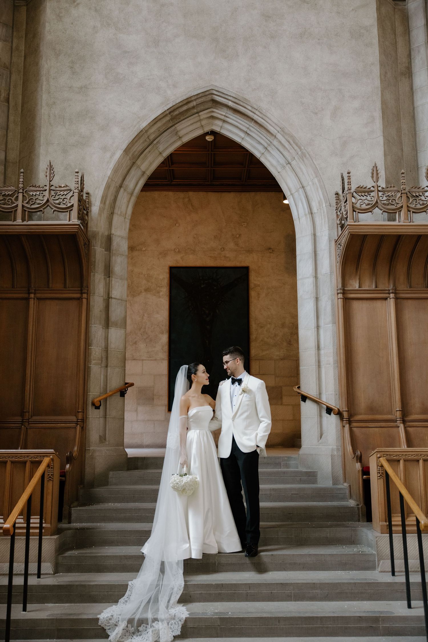 A wedding couple shares an intimate moment in an elegant archway corridor of a historic stone building.