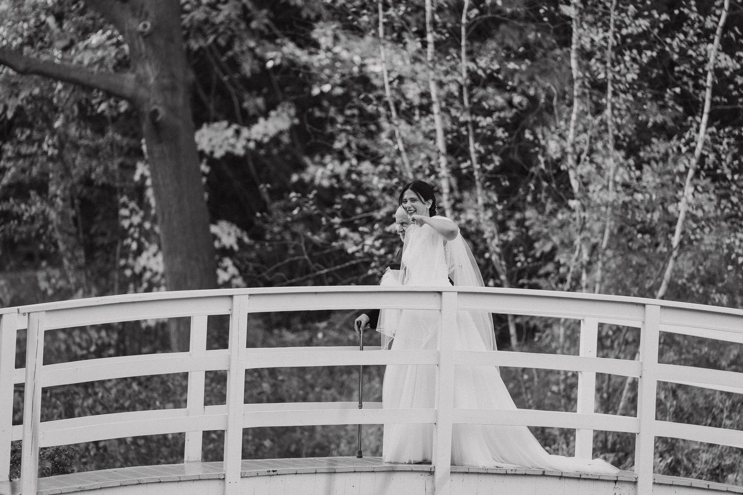 Black and white photo of a couple standing on a curved white bridge.