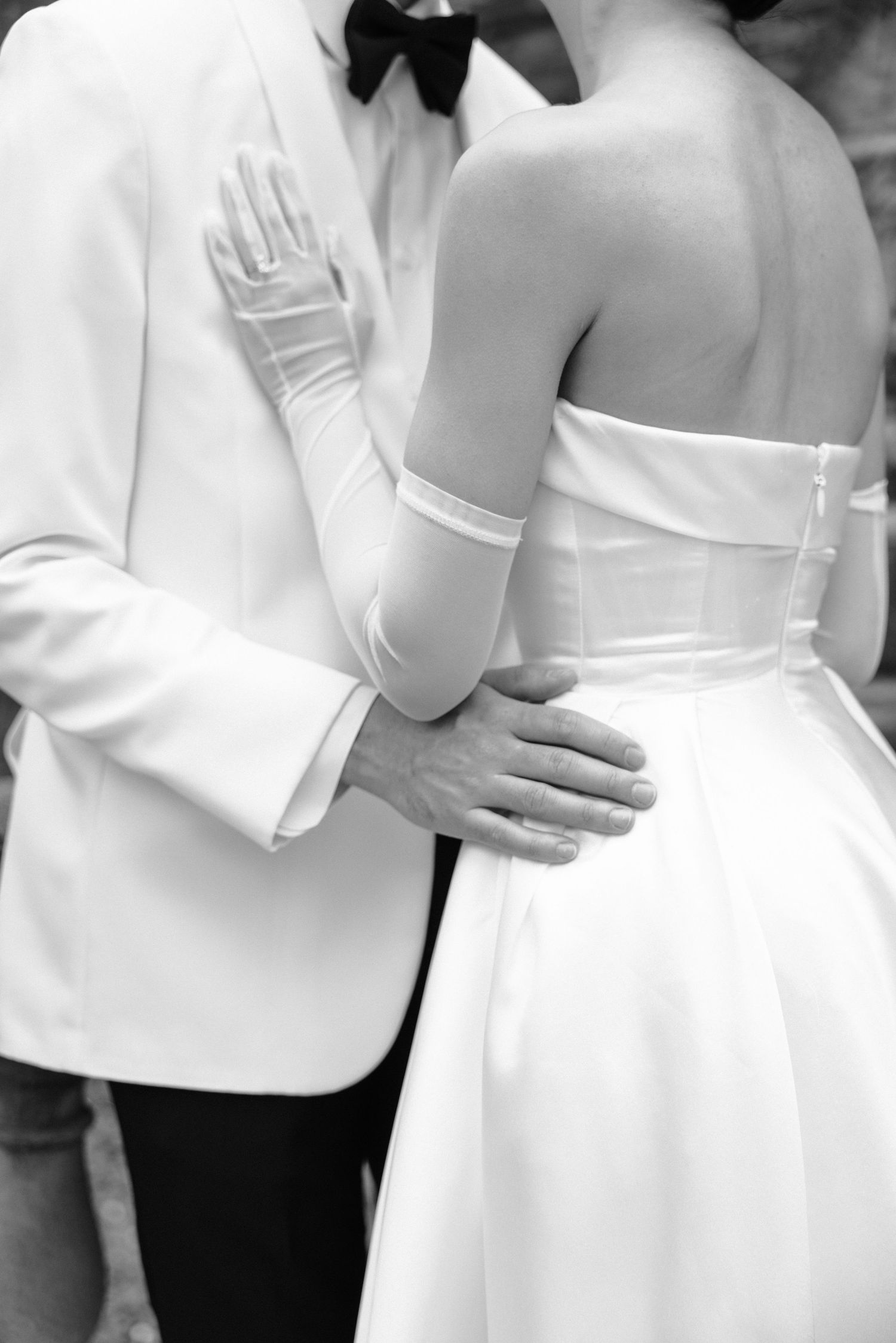 A close-up black and white photo of newlyweds embracing, showing the bride's white dress and groom's formal suit.