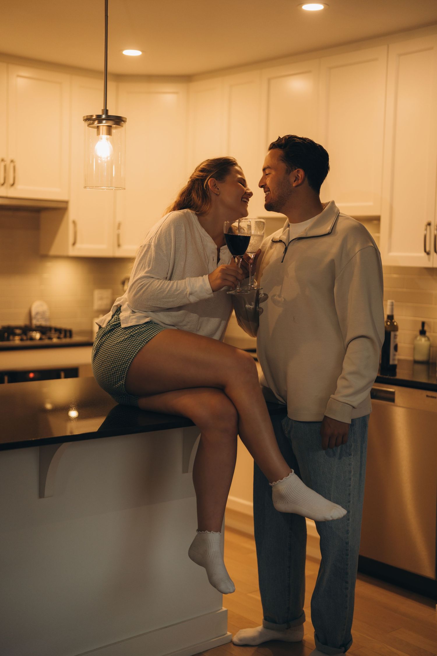 A couple embraces in a dimly lit kitchen with warm lighting, creating an intimate moment together.