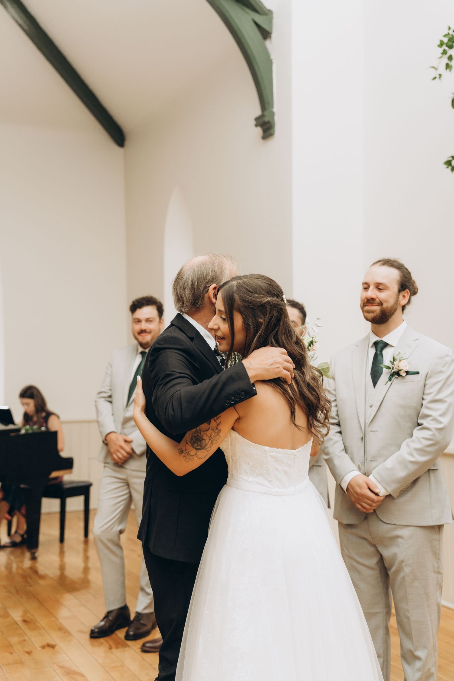 Wedding couple shares a tender dance moment while guests watch from the sides in a bright indoor venue.