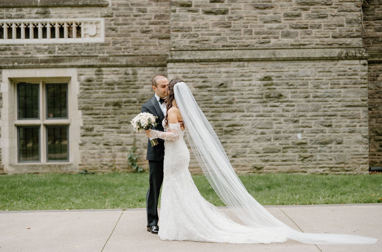 A long flowing white wedding veil trails behind on stone steps during a formal ceremony.