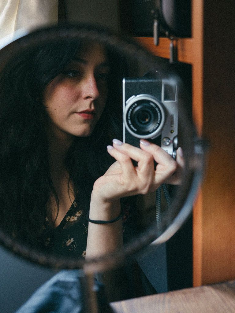 A series of self-portrait mirror reflections showing someone taking photos with a vintage camera in warm lighting.