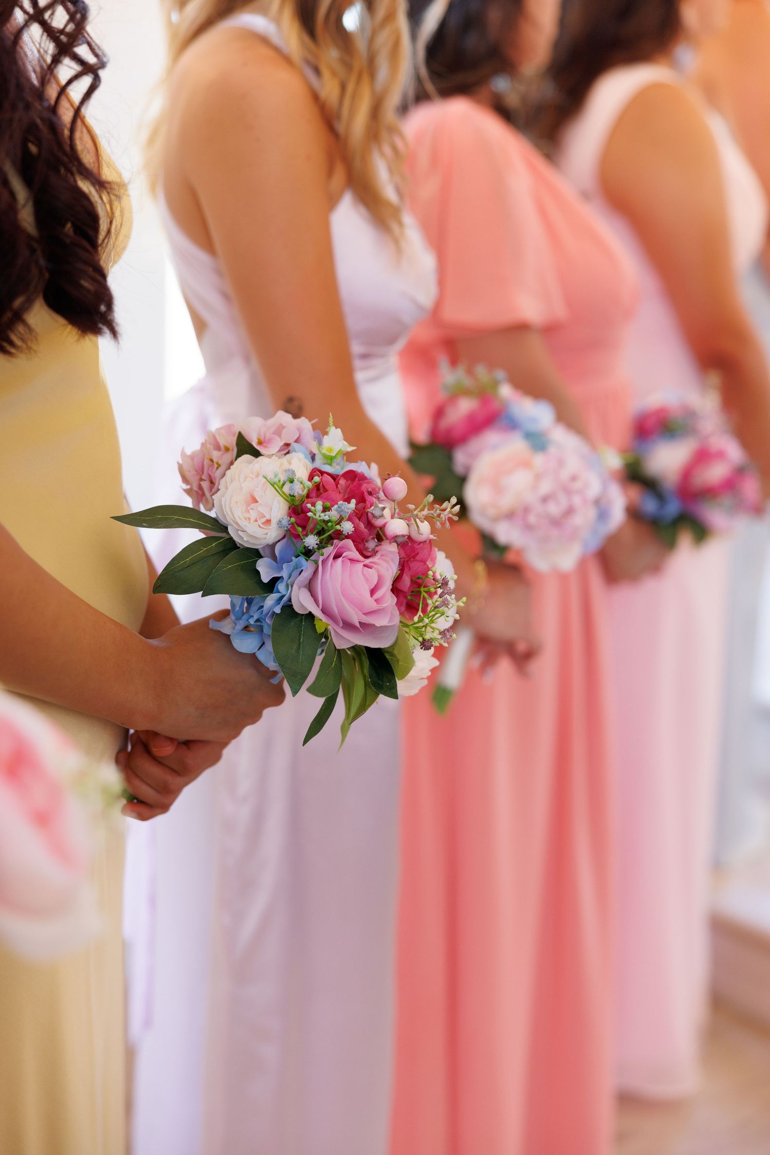 Bridesmaids holding pink and white floral bouquets lined up in pastel dresses.