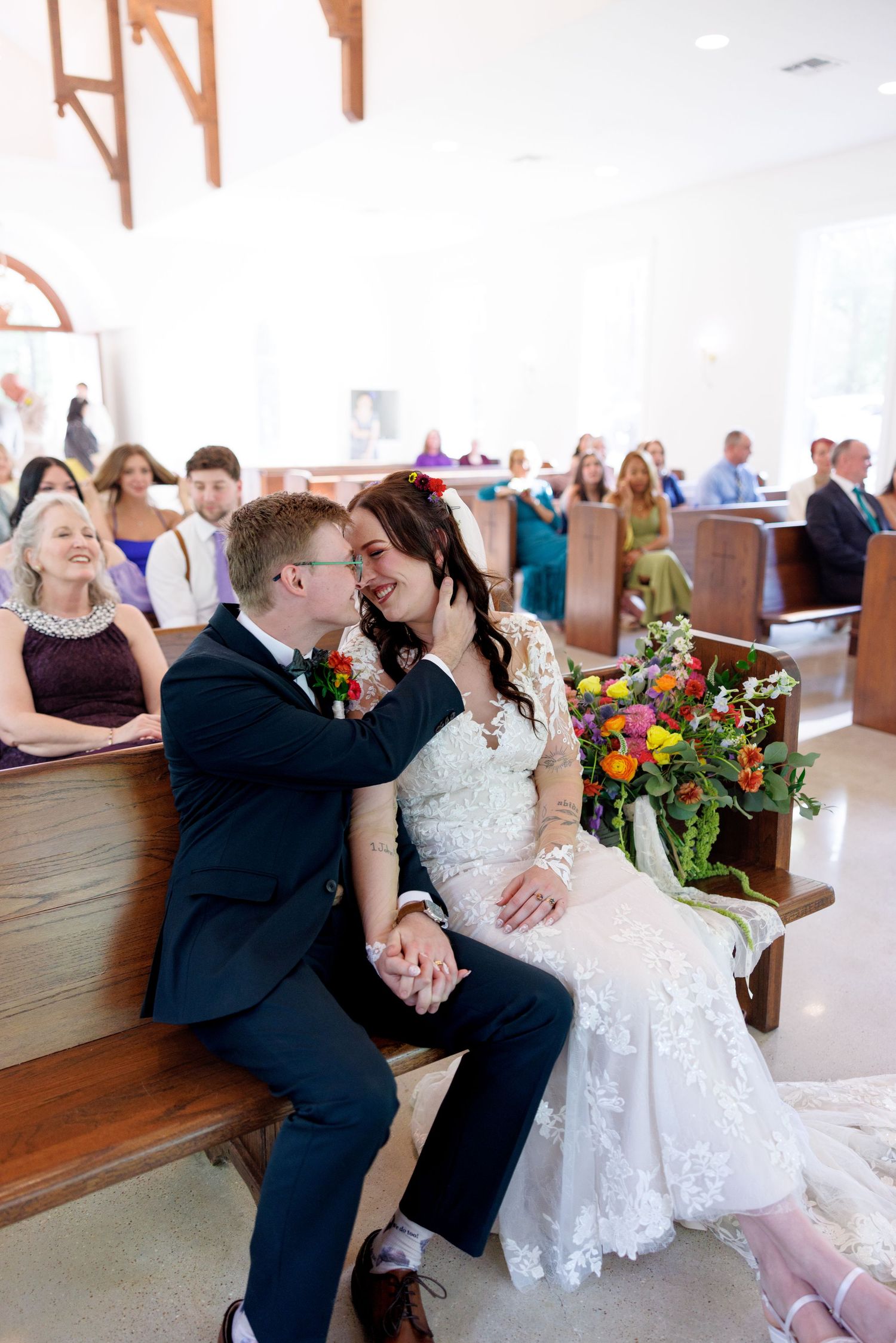 Bride and groom share an intimate moment holding hands on a church pew during their wedding ceremony.