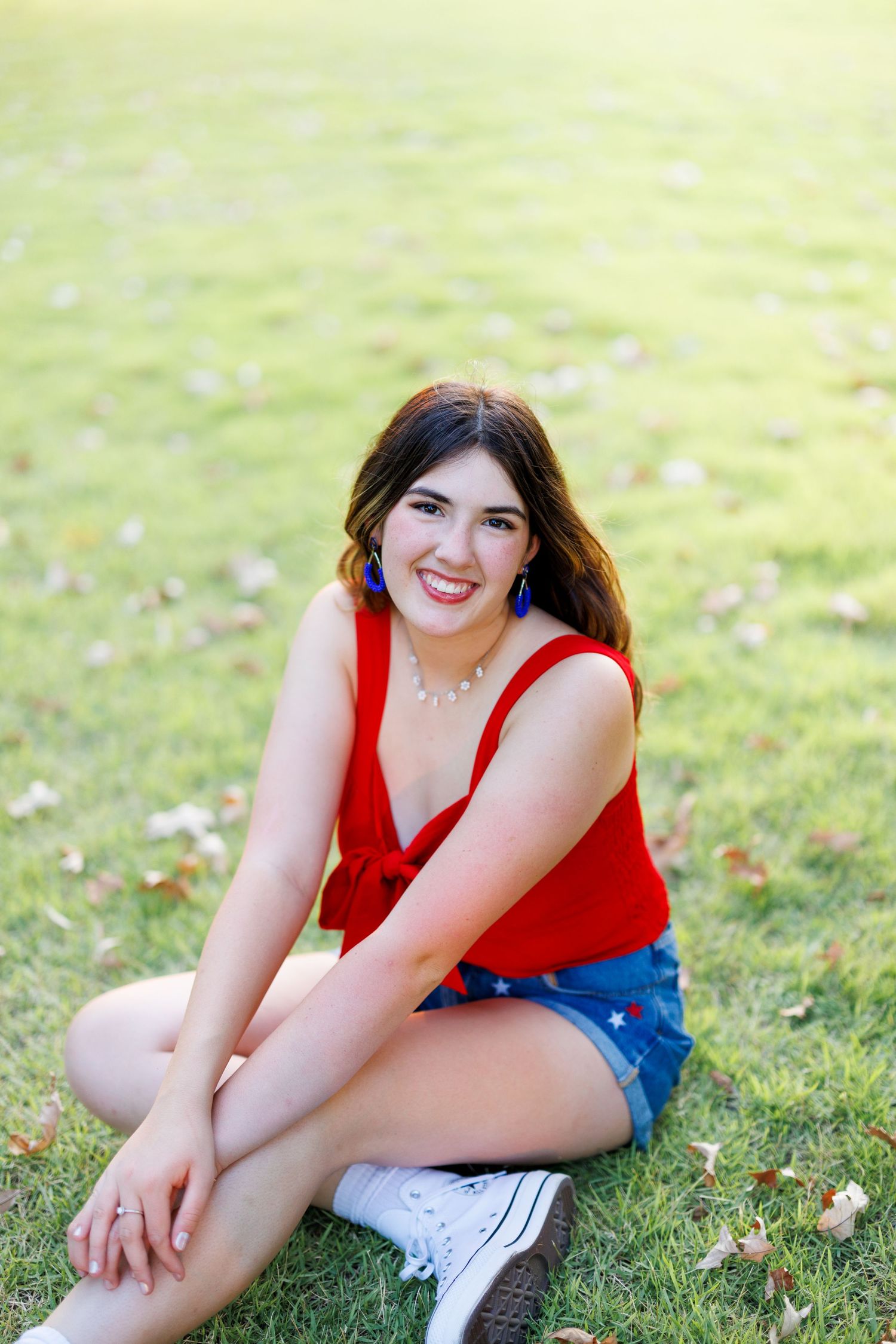 Person in casual summer outfit smiles while sitting on green grass.