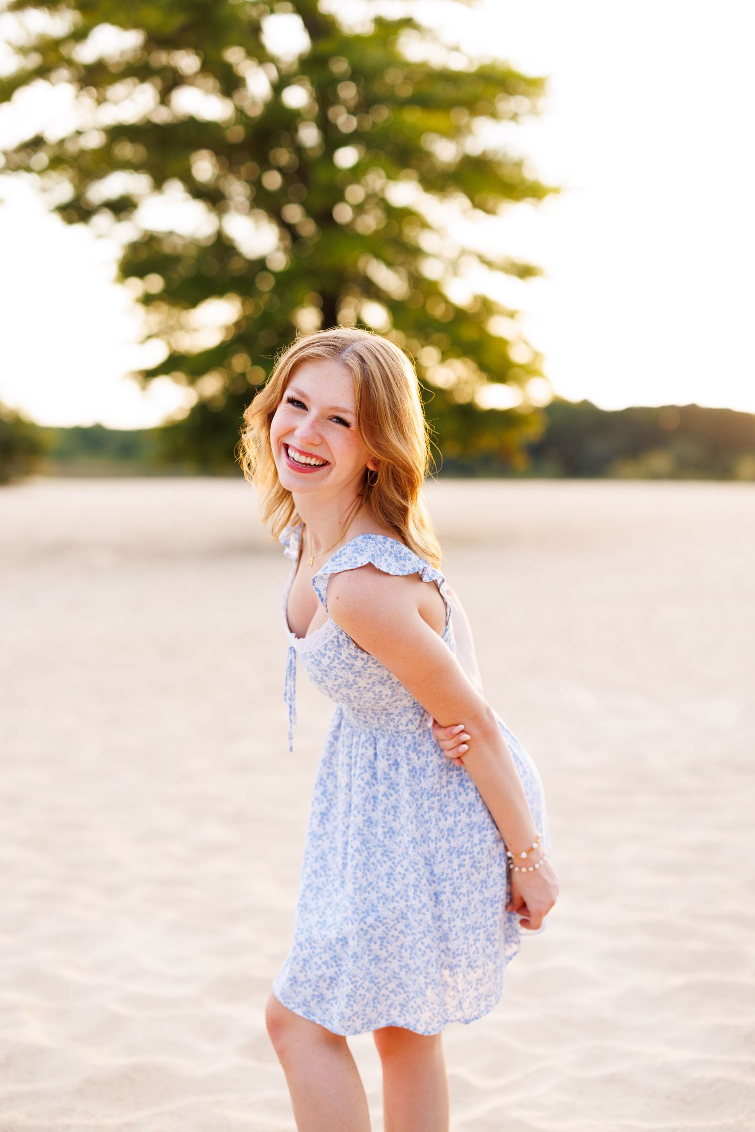 Person in a light blue floral dress playing and twirling on a sunny beach.