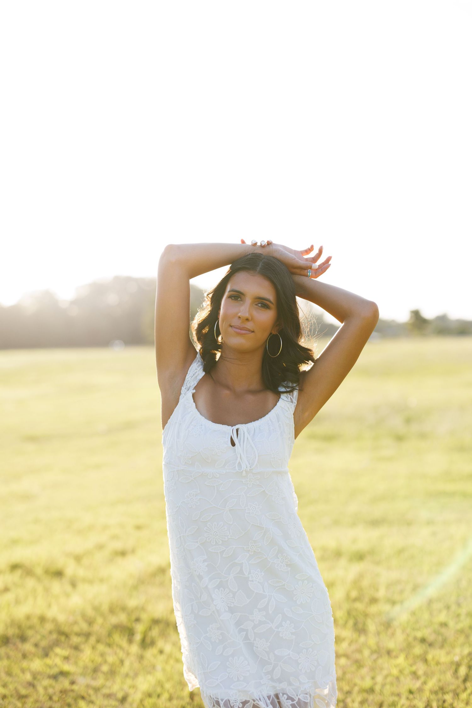 Person in white lace top posing gracefully in a sunlit meadow.