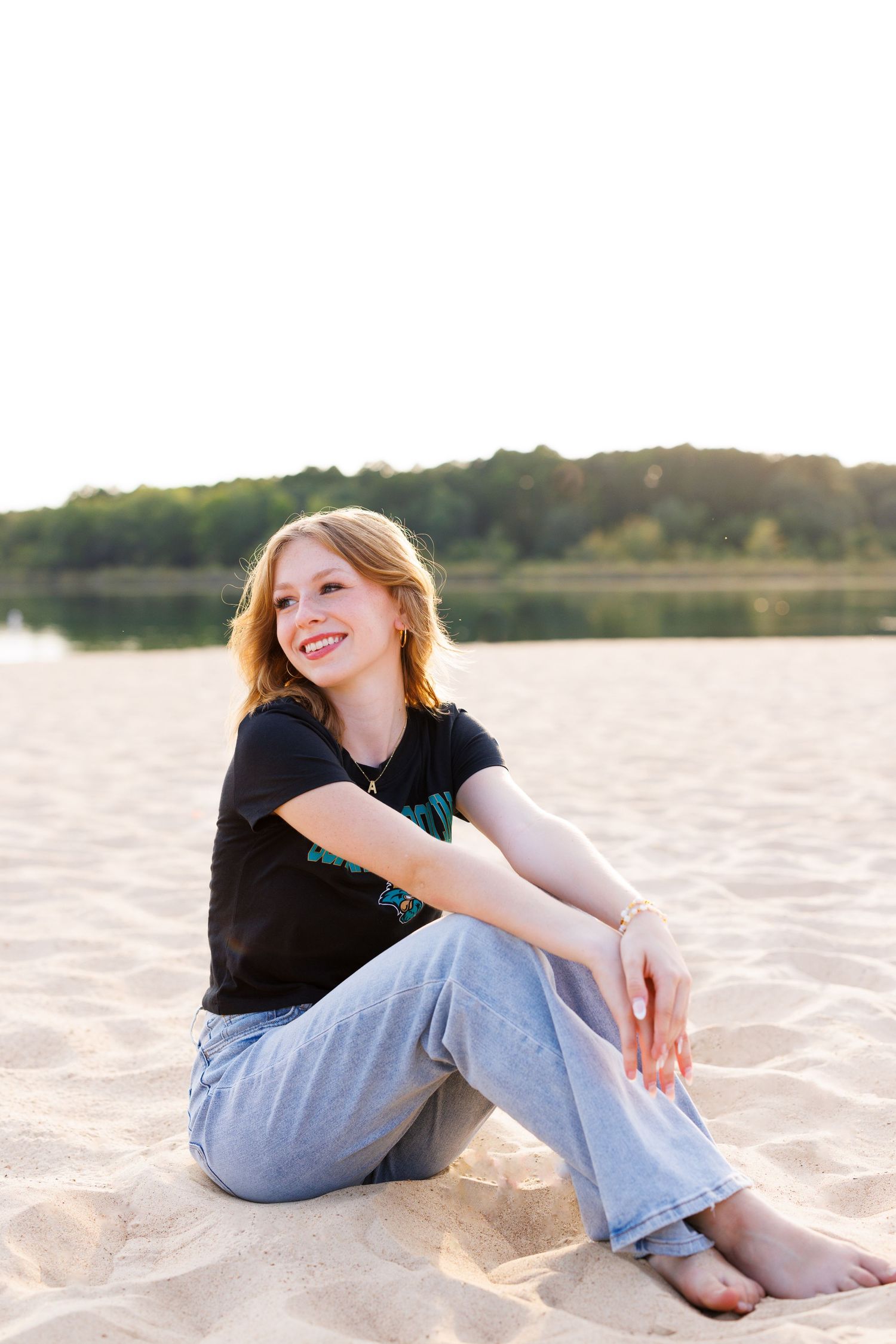 Person relaxes on sandy beach wearing casual outfit against waterfront backdrop.