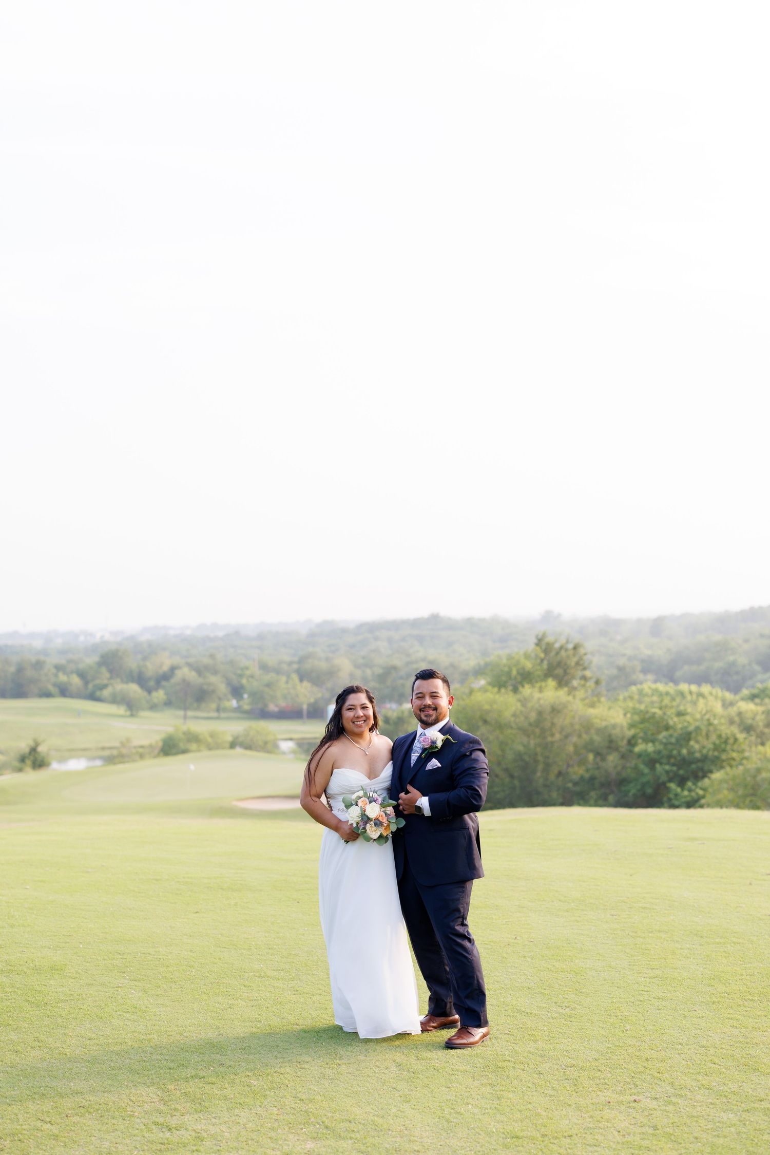 Bride and groom posing together on a scenic golf course, bride holding a bouquet on their wedding day.