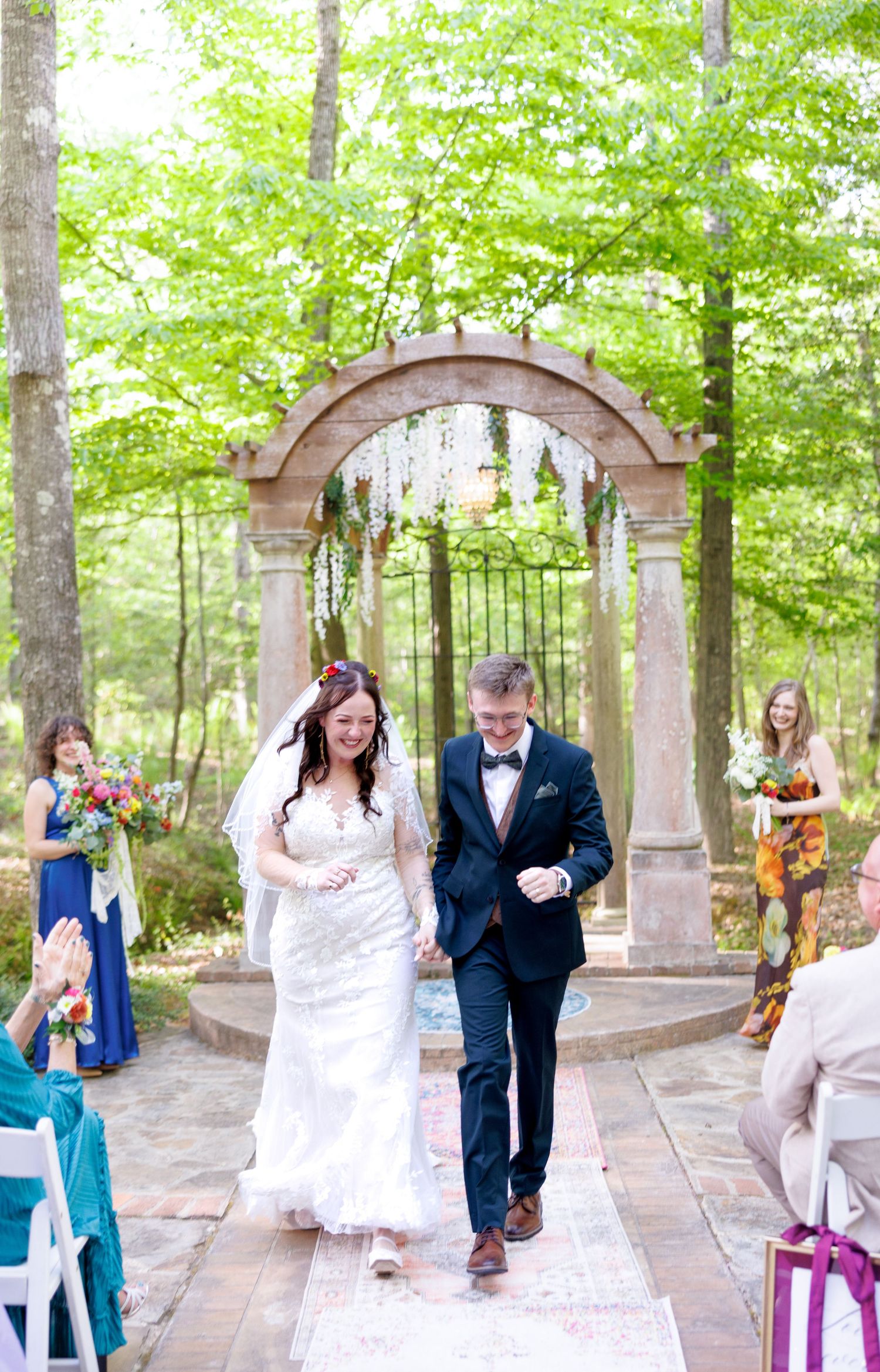 Newlyweds walk joyfully back down the aisle after their outdoor forest wedding ceremony.