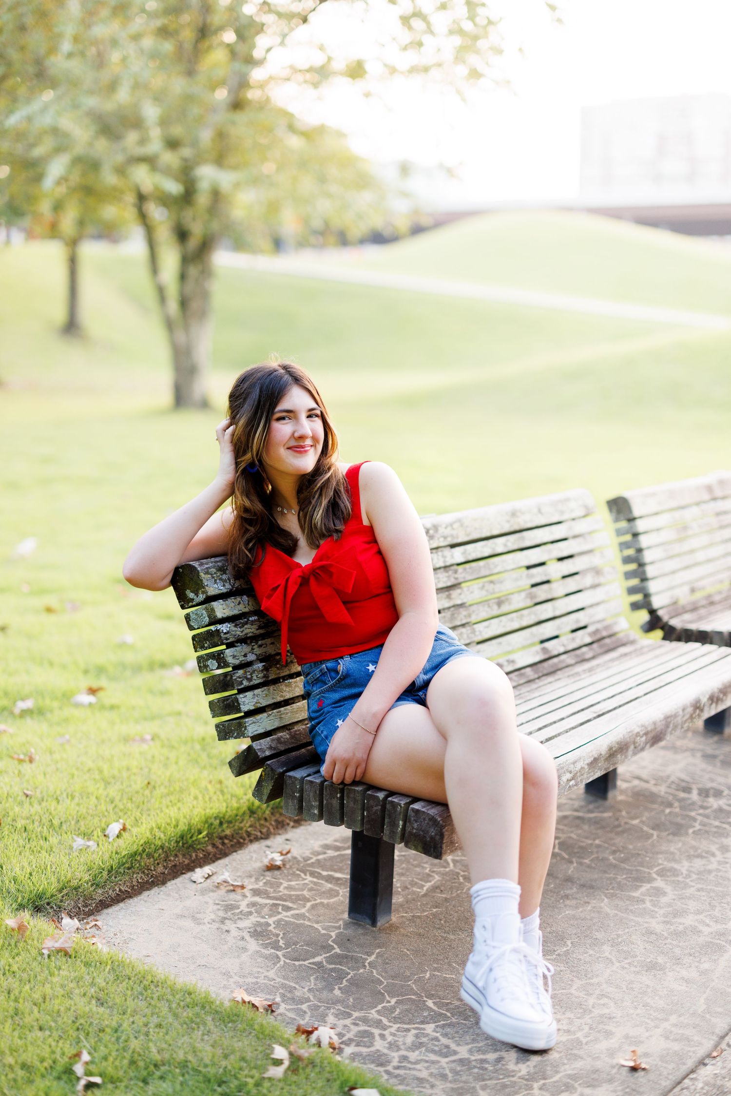 Person in red top and shorts sits casually on park bench during summer photoshoot.