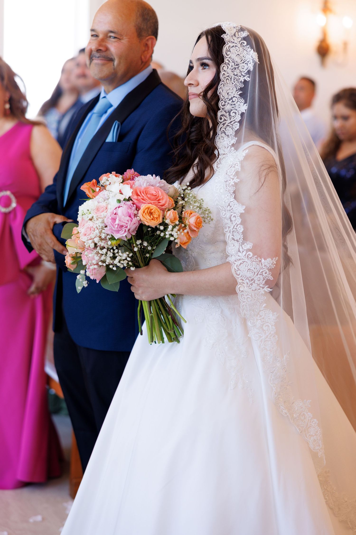 Wedding party members stand in formation during ceremony with bright floral bouquets.