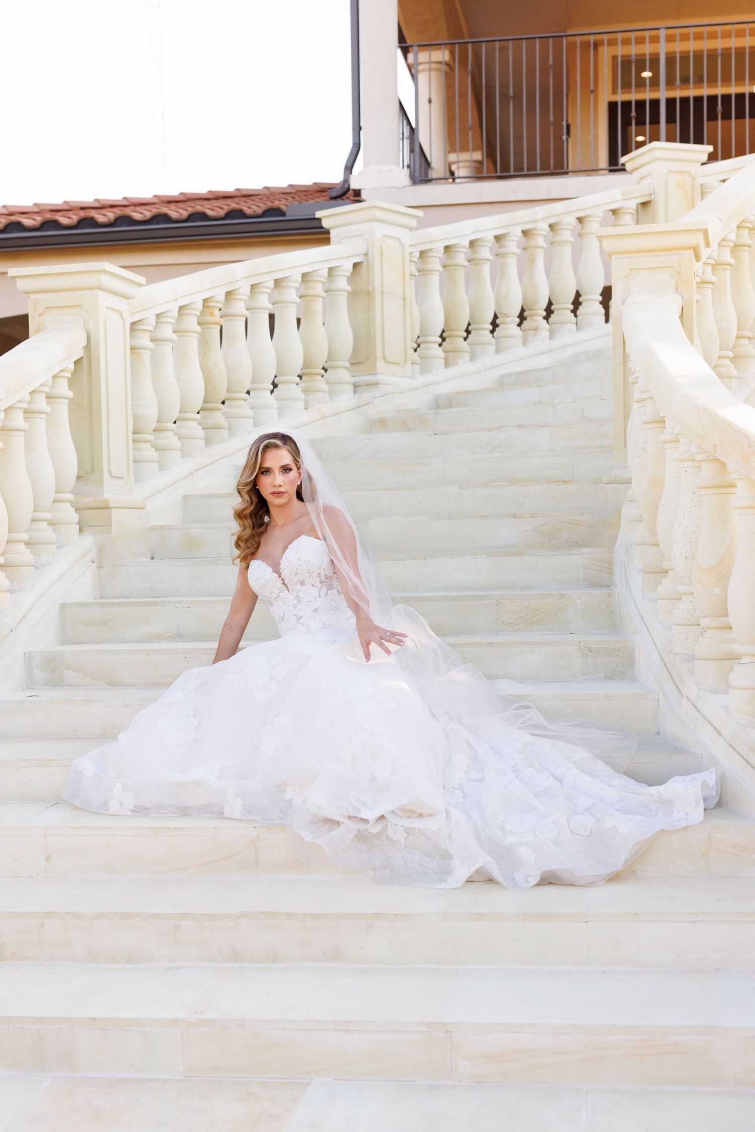 A bride in a flowing white gown poses gracefully on elegant white marble steps.