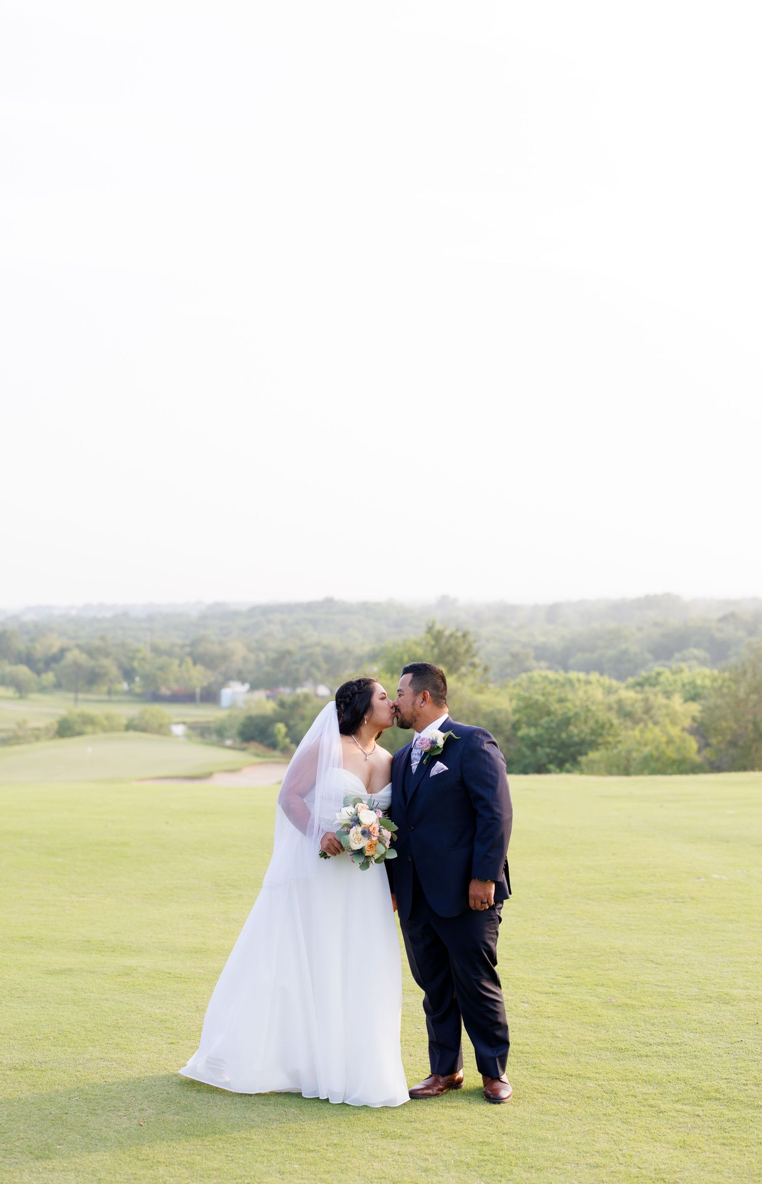 Bride and groom sharing a tender kiss on a golf course with a beautiful rolling green landscape.