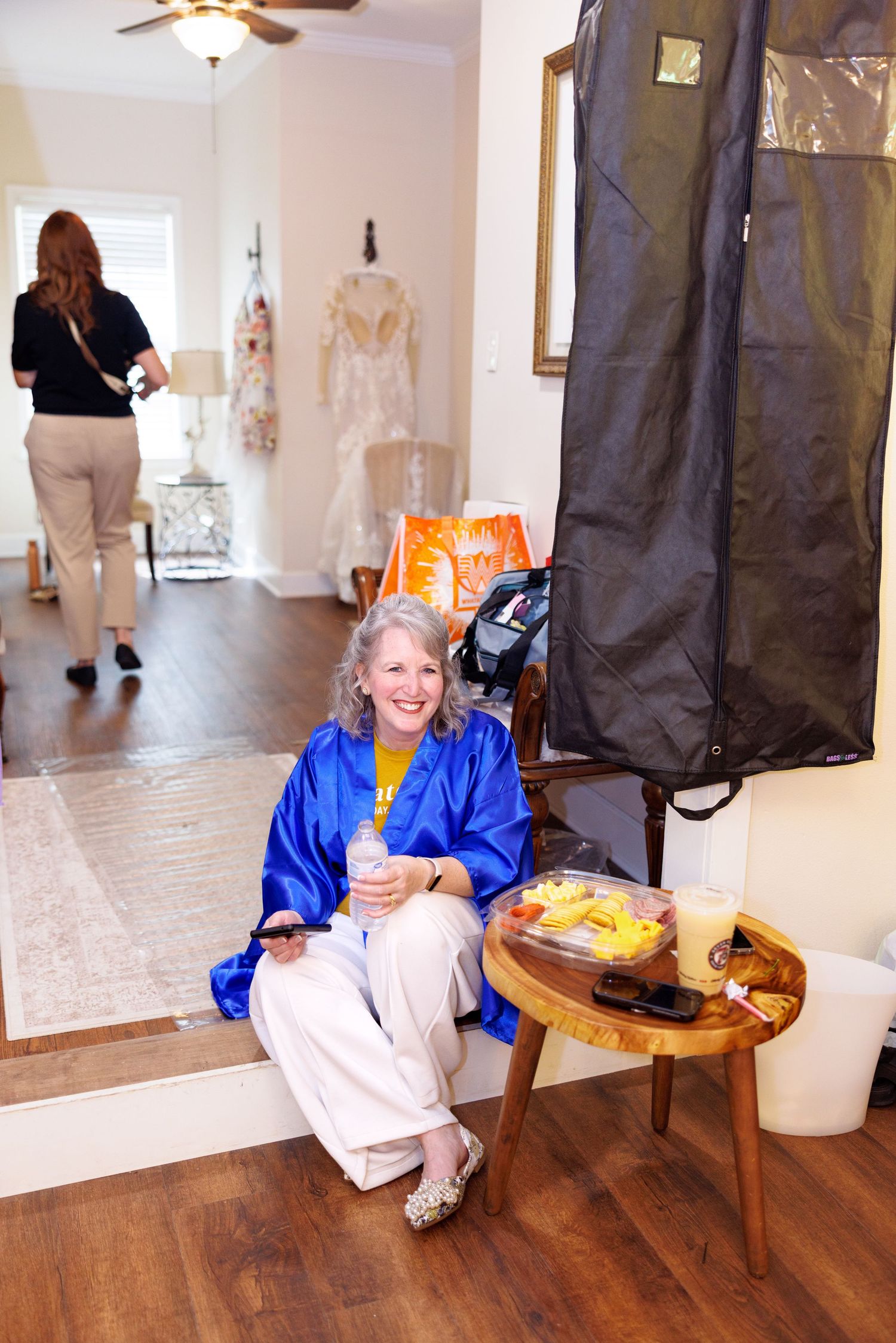 Woman in blue robe smiles while sitting during wedding preparation in bright room.