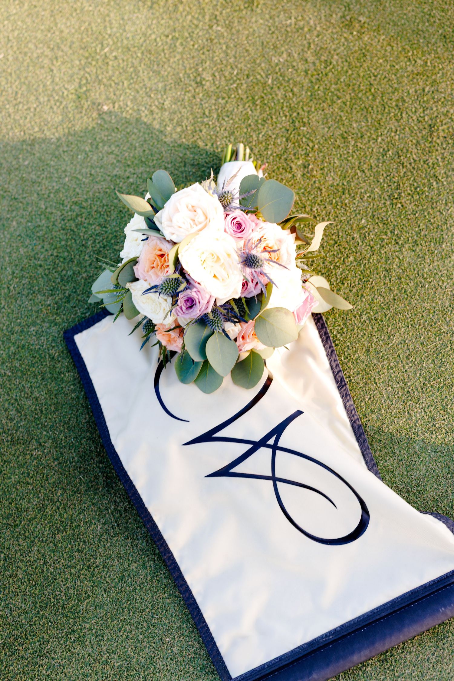 Bridal bouquet with pink and white roses on a monogrammed white banner on green grass.