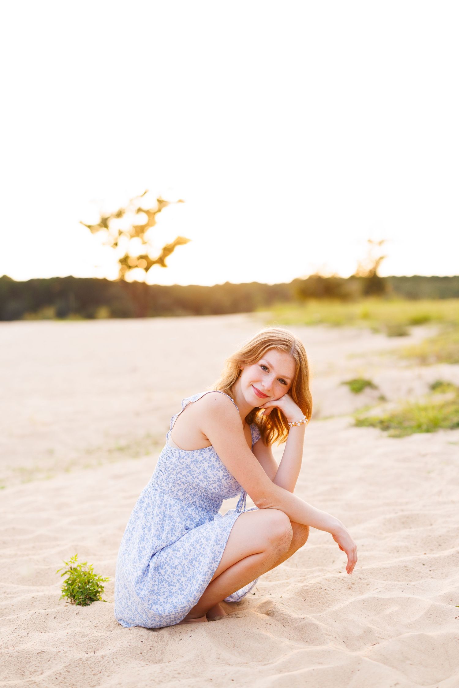 Person in blue floral dress poses elegantly on beach during golden hour.