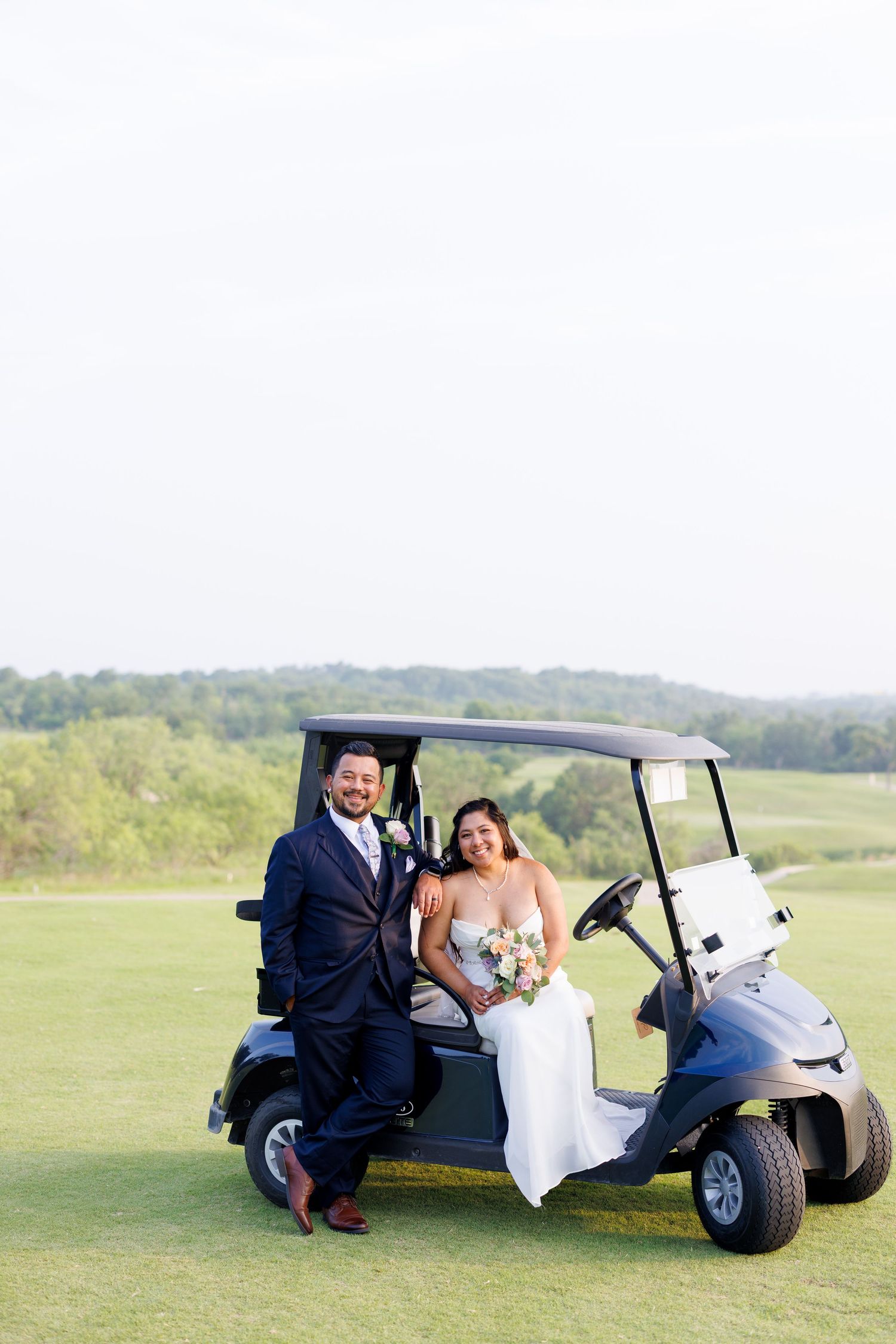 Bride and groom posing with a golf cart on a lush green golf course on their wedding day.