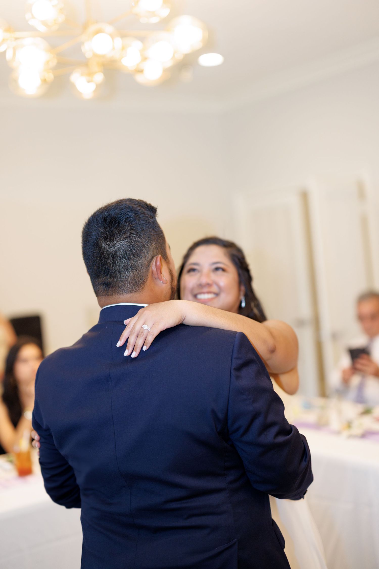 Bride and groom share their first dance at wedding reception, bride smiling joyfully with arm around groom's shoulder.