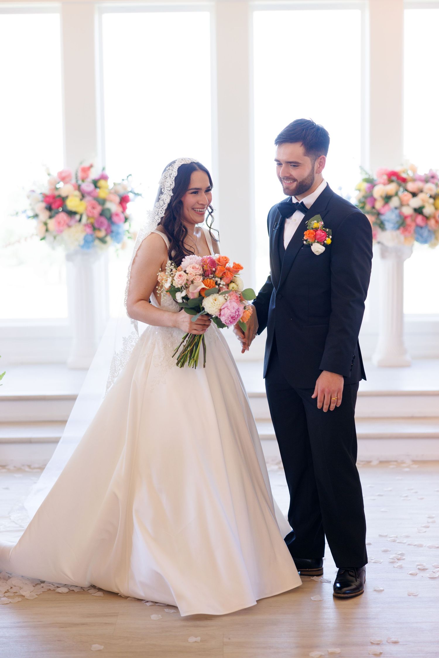 Wedding couple poses together in a bright white room with colorful floral arrangements.