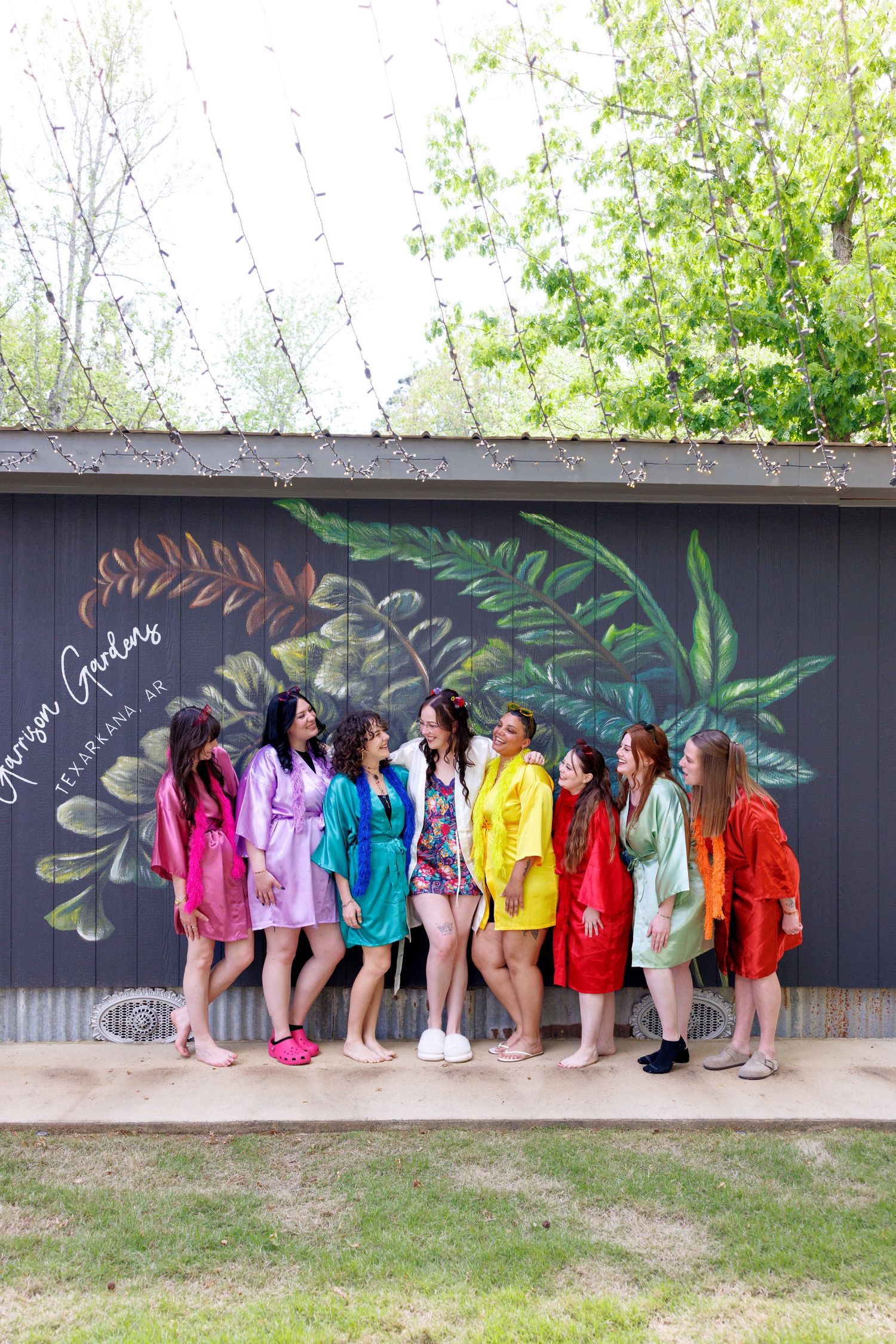 A group of bridesmaids wearing colorful robes pose together in front of a floral mural at Georgia Gardens venue.