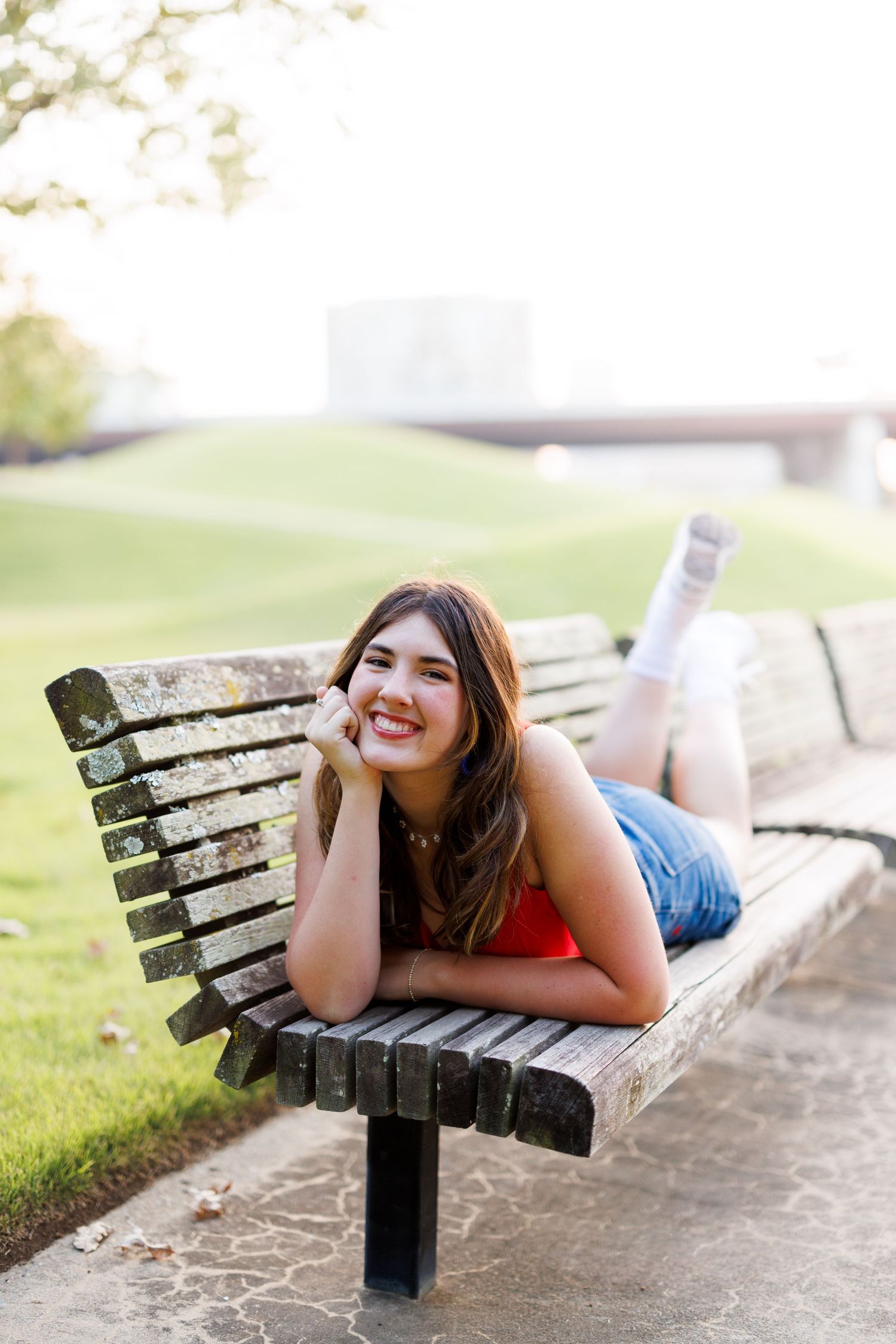 Person lying relaxed on wooden park bench during outdoor photo session.