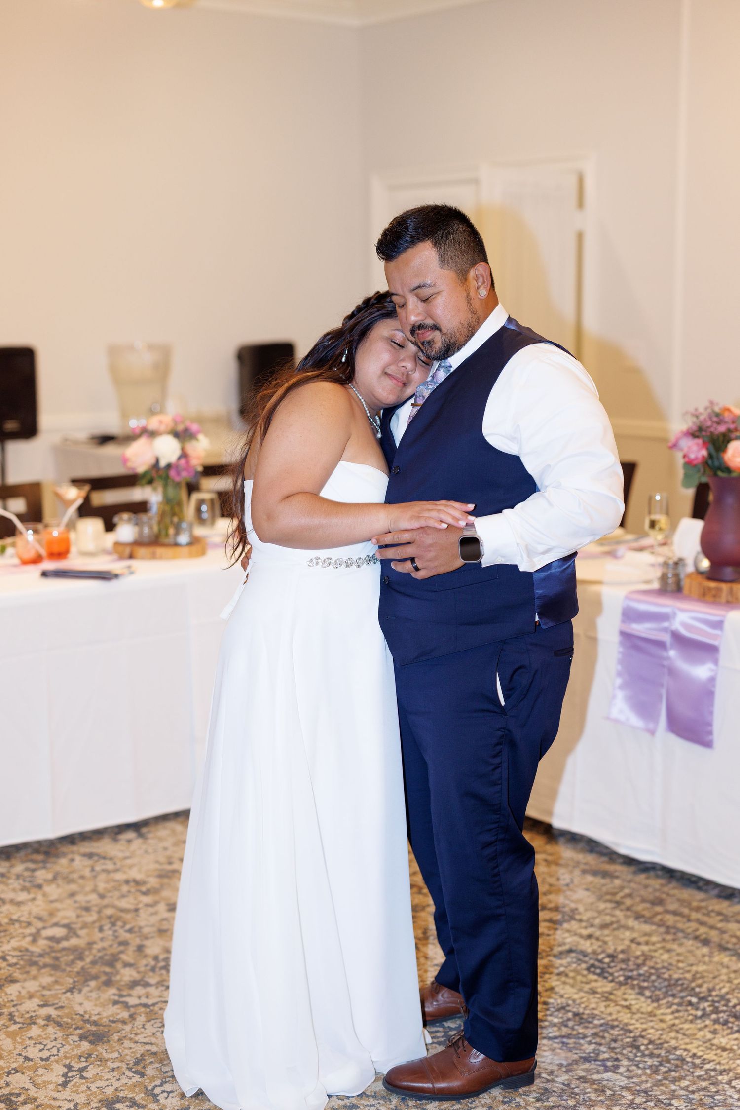 Bride and groom share emotional first dance embrace at wedding reception in decorated venue.