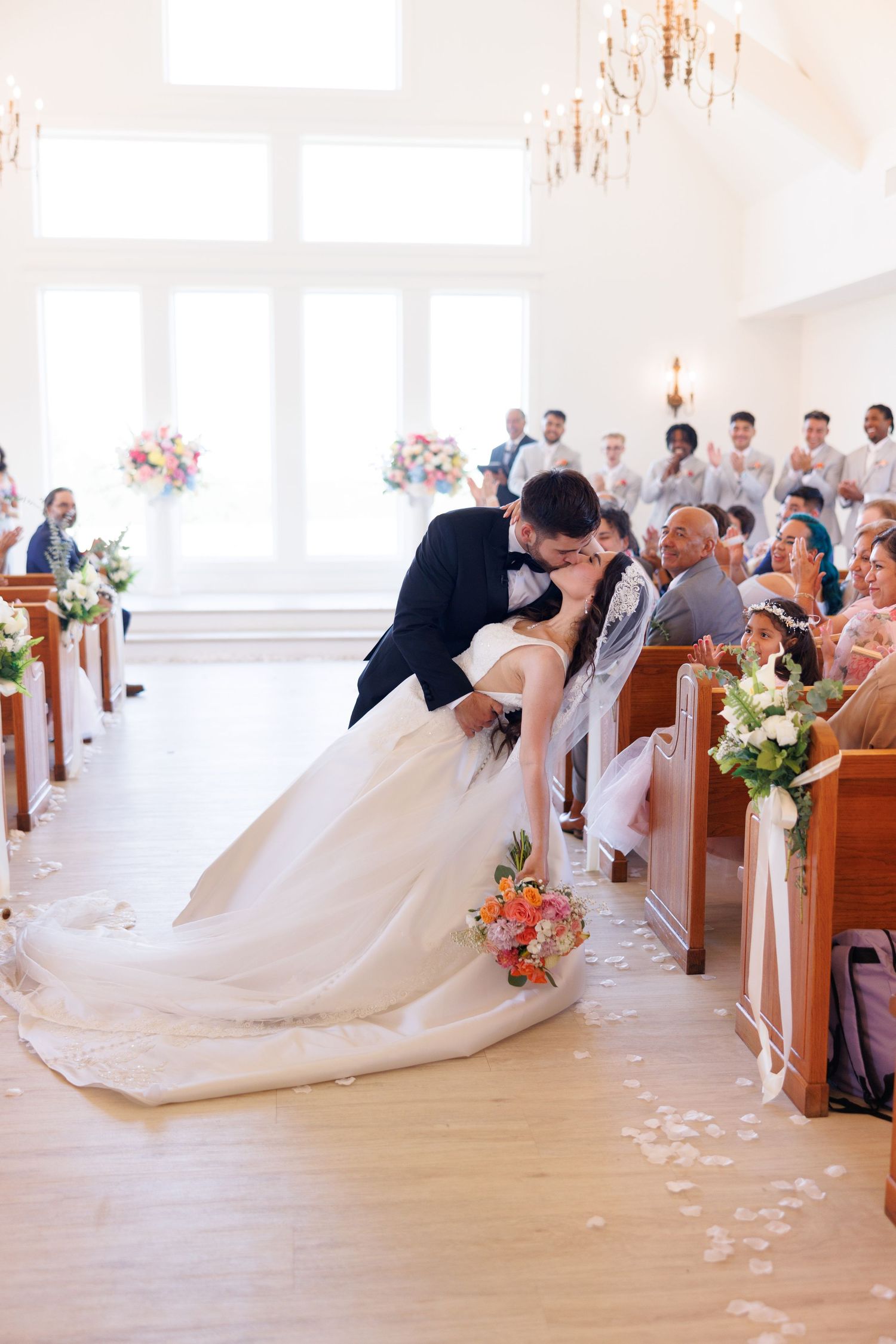 A romantic dip kiss during the wedding ceremony as guests look on from wooden pews.