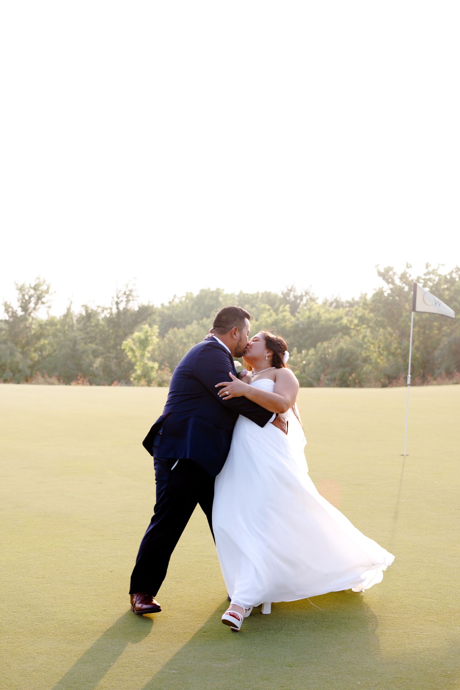 Bride and groom sharing a romantic kiss on a golf course green during their outdoor wedding celebration.
