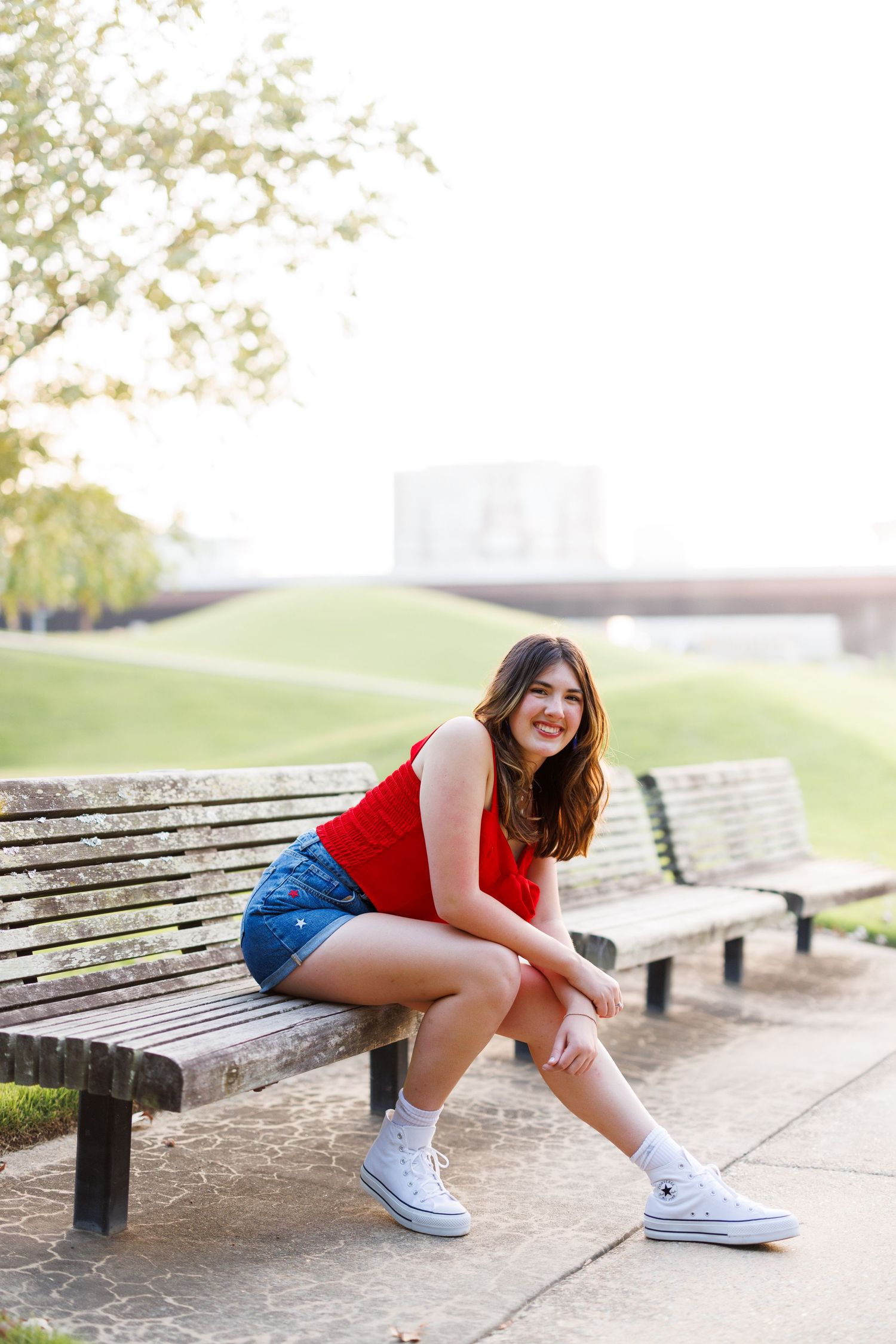 Person in red top and denim shorts posing playfully near park benches.