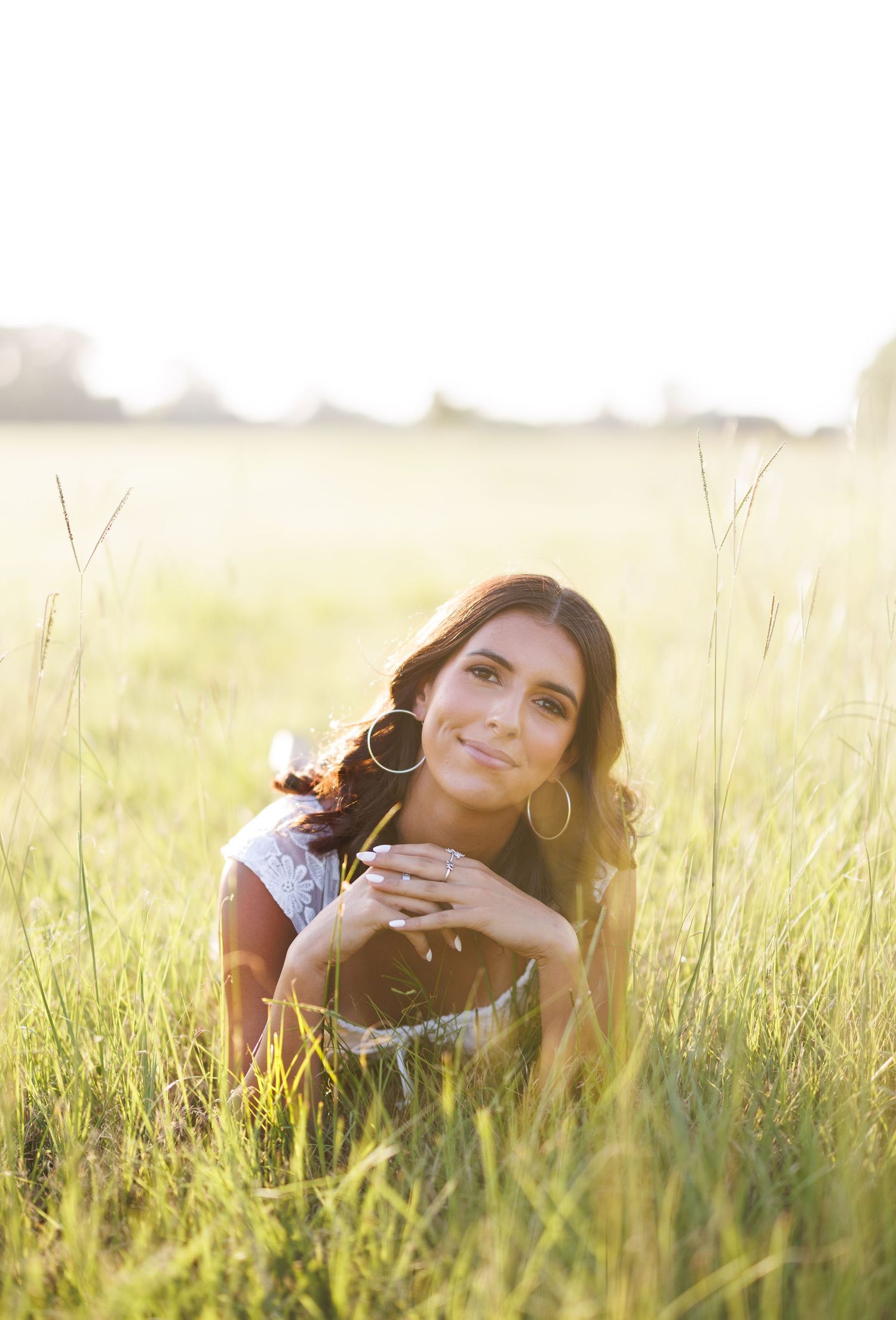 Person lying in tall grass during golden sunset with dreamy lighting.