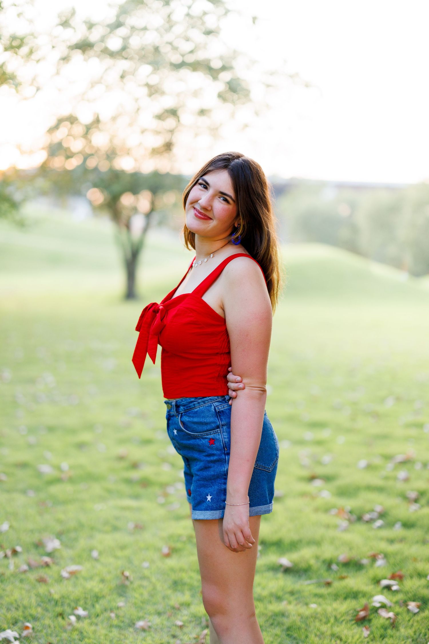 Person in red tank top and denim shorts poses playfully outdoors.