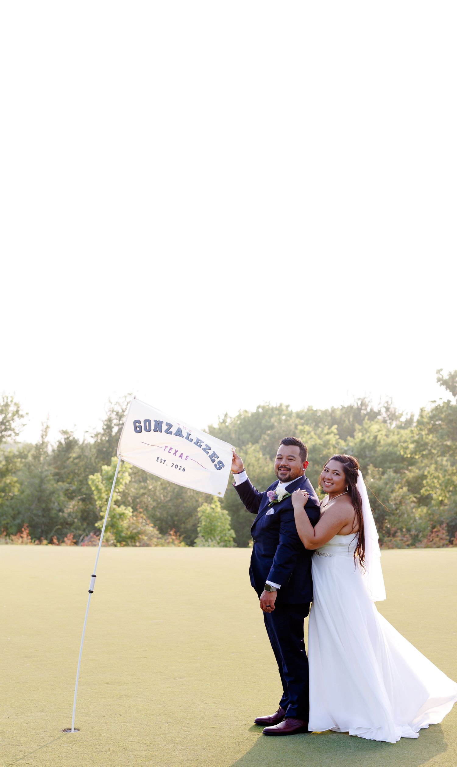 Bride and groom posing with a custom Gonzalez wedding flag on a golf course green on their wedding day.