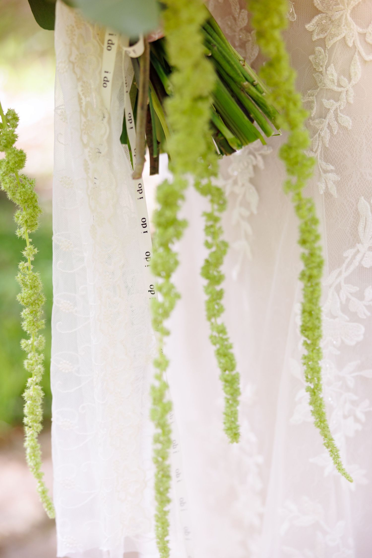 Close-up of bridal bouquet with cascading green amaranthus against white lace wedding dress.