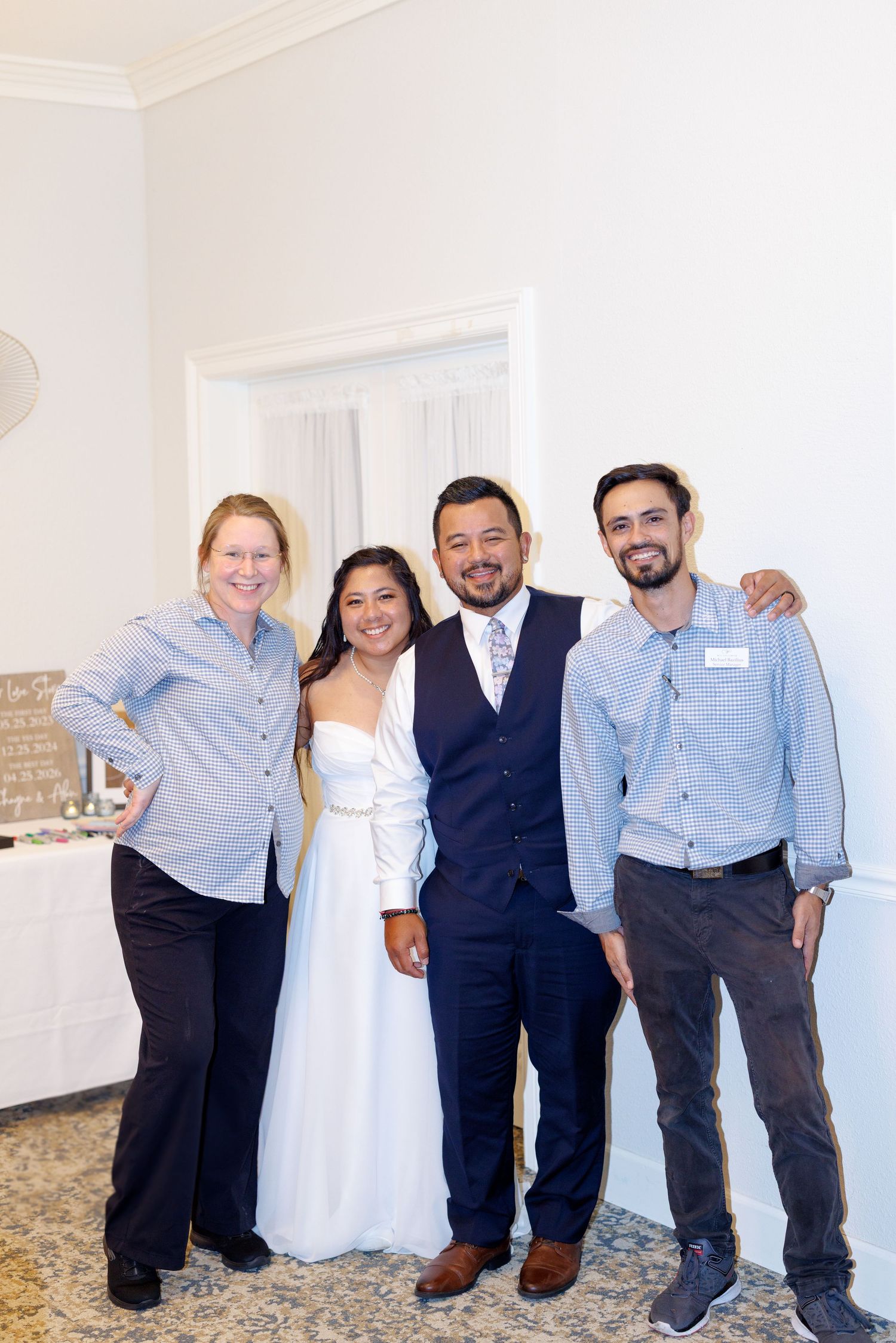 Bride and groom posing with two guests at a wedding reception, smiling together in elegant attire.
