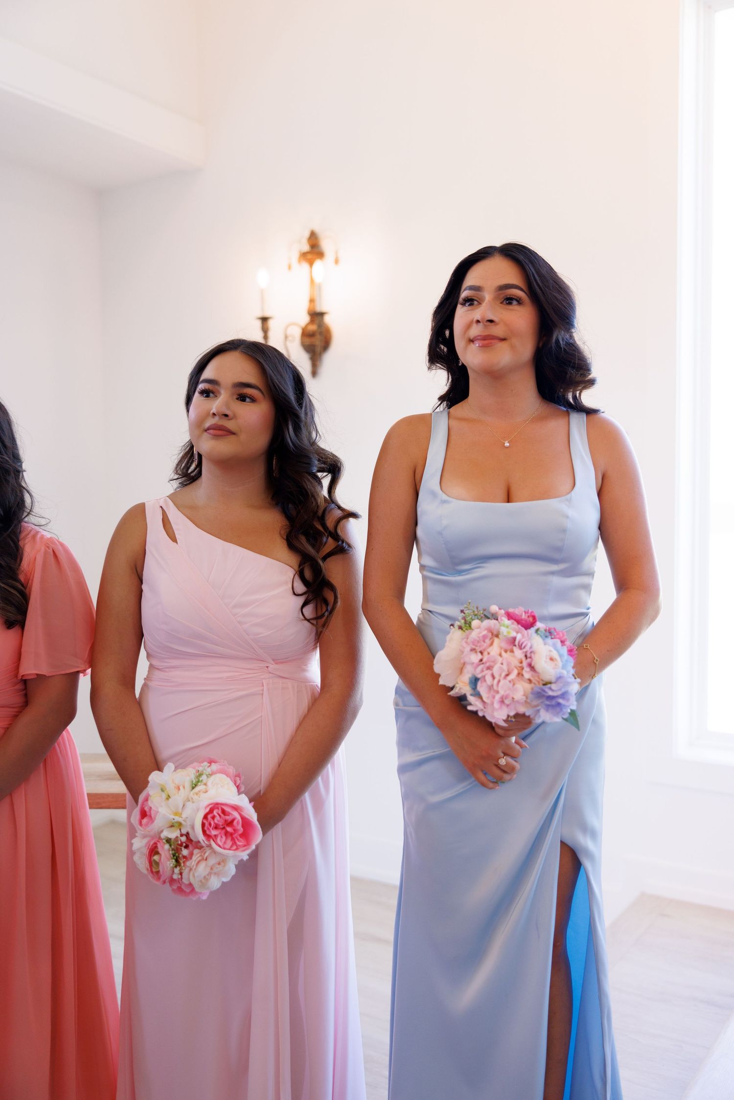 Bridesmaids in pastel dresses holding pink and white bouquets stand in formation.