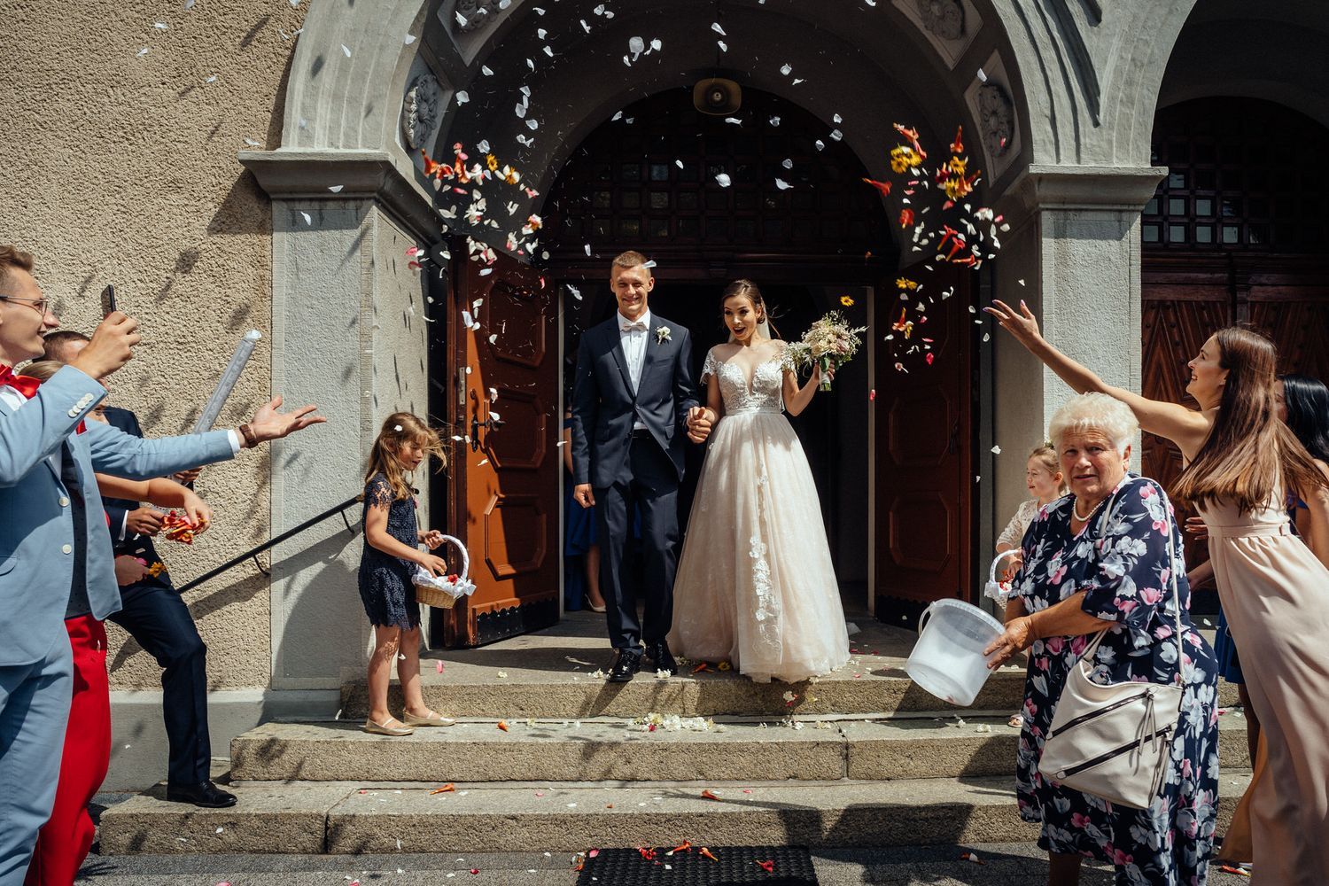 Wyjście pary młodej z kościoła pod deszczem płatków róż, profesjonalna fotografia ślubna opolskie.