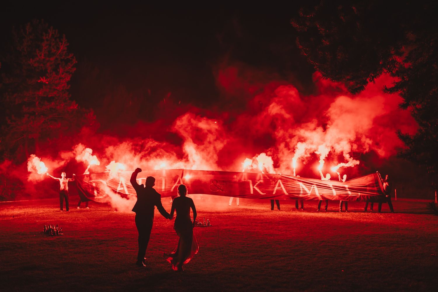 Nocne zdjęcie pary młodej z czerwonymi racami dymnymi, efektowne ujęcie z filmu ślubnego.