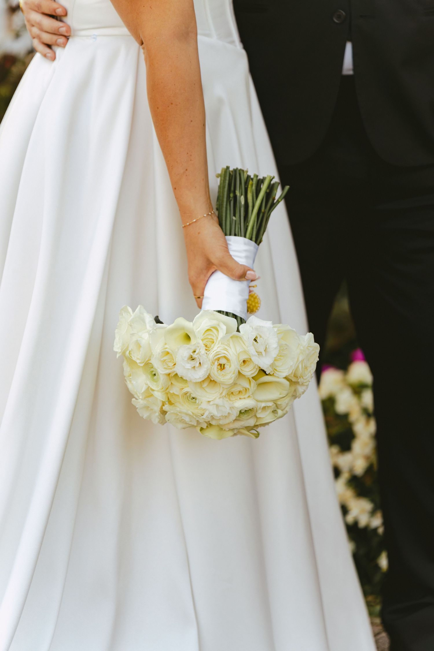 Bride holds a stunning white rose bouquet wrapped in white ribbon against her elegant satin wedding gown.