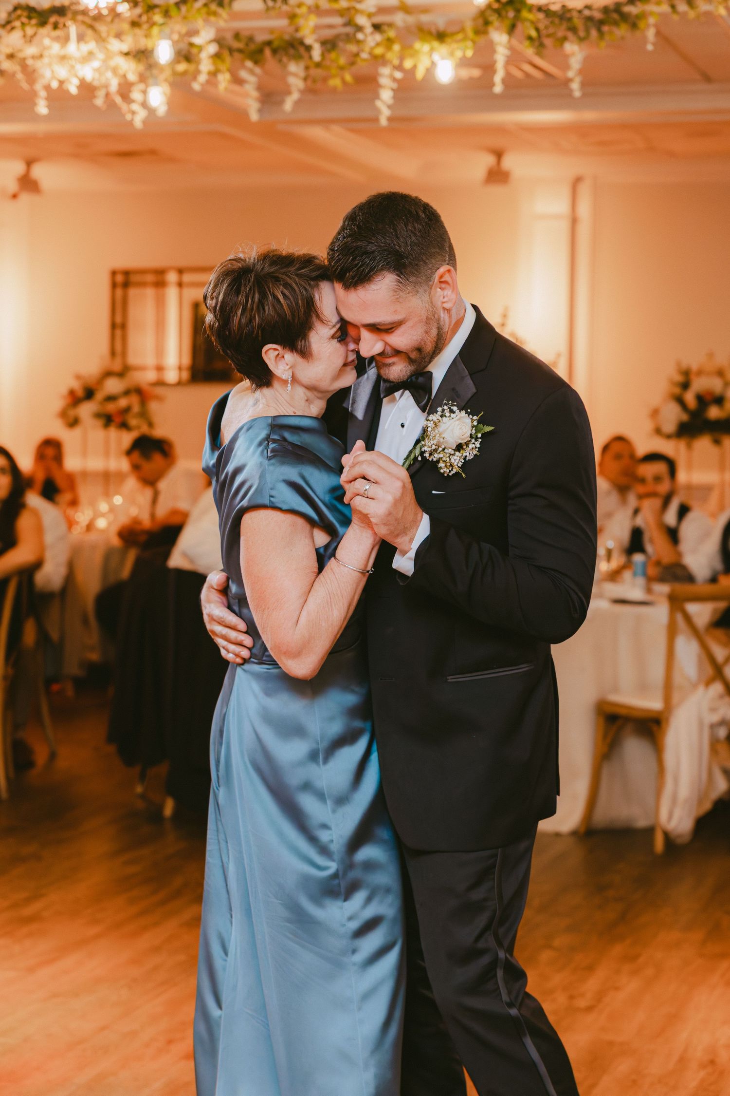 Mother and son sharing an emotional first dance at a warmly lit wedding reception venue.