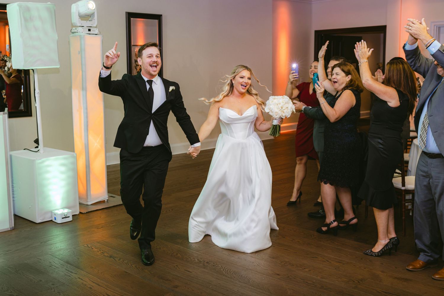 Excited bride and groom make a grand entrance into their wedding reception as guests cheer.