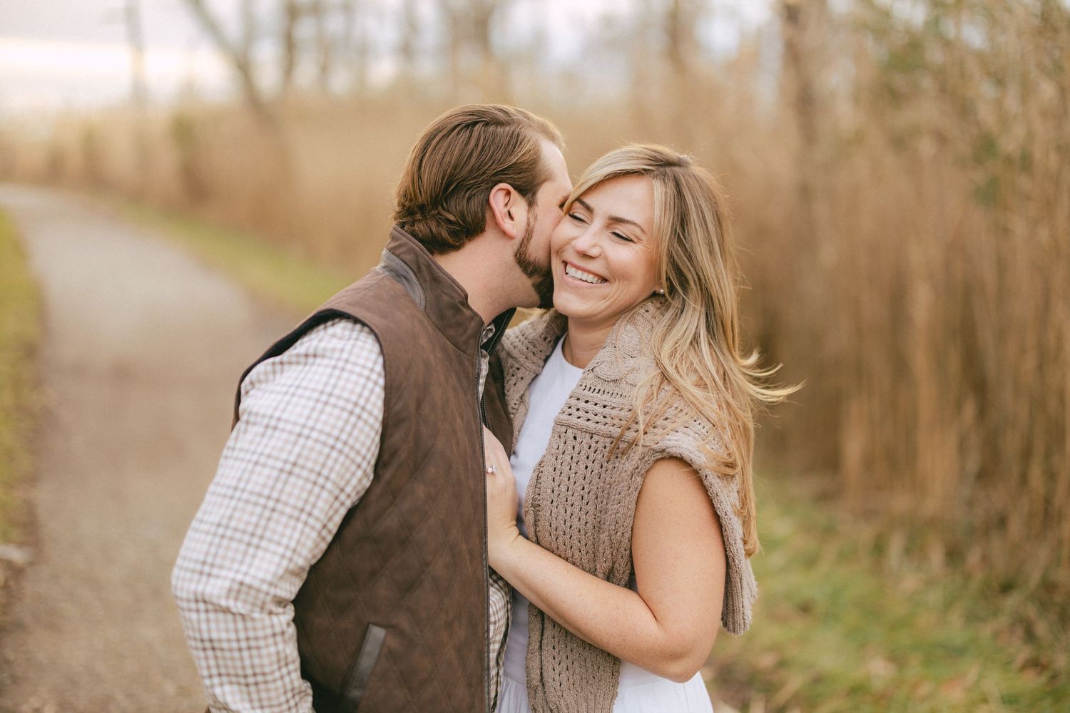 Man kissing smiling woman on the cheek outdoors on a scenic fall nature path.