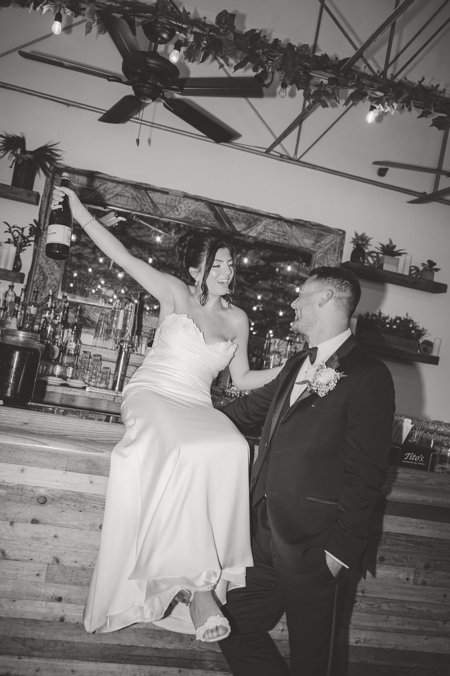 Bride and groom dance joyfully at a rustic bar venue, bride raising her arm in celebration.