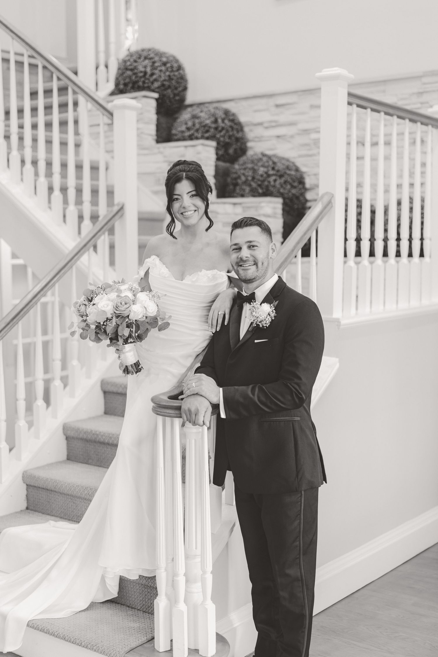 Bride and groom pose elegantly on a staircase in black and white wedding portrait.