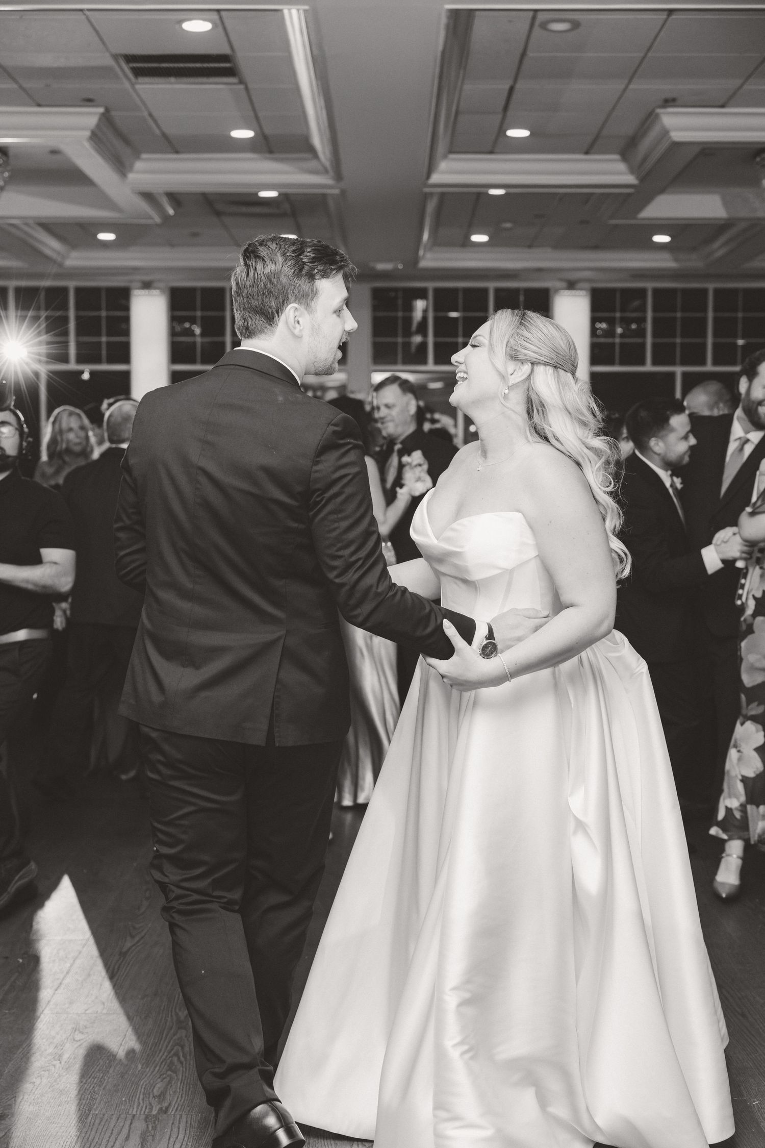 Black and white photo of bride and groom laughing together while dancing at their wedding reception.