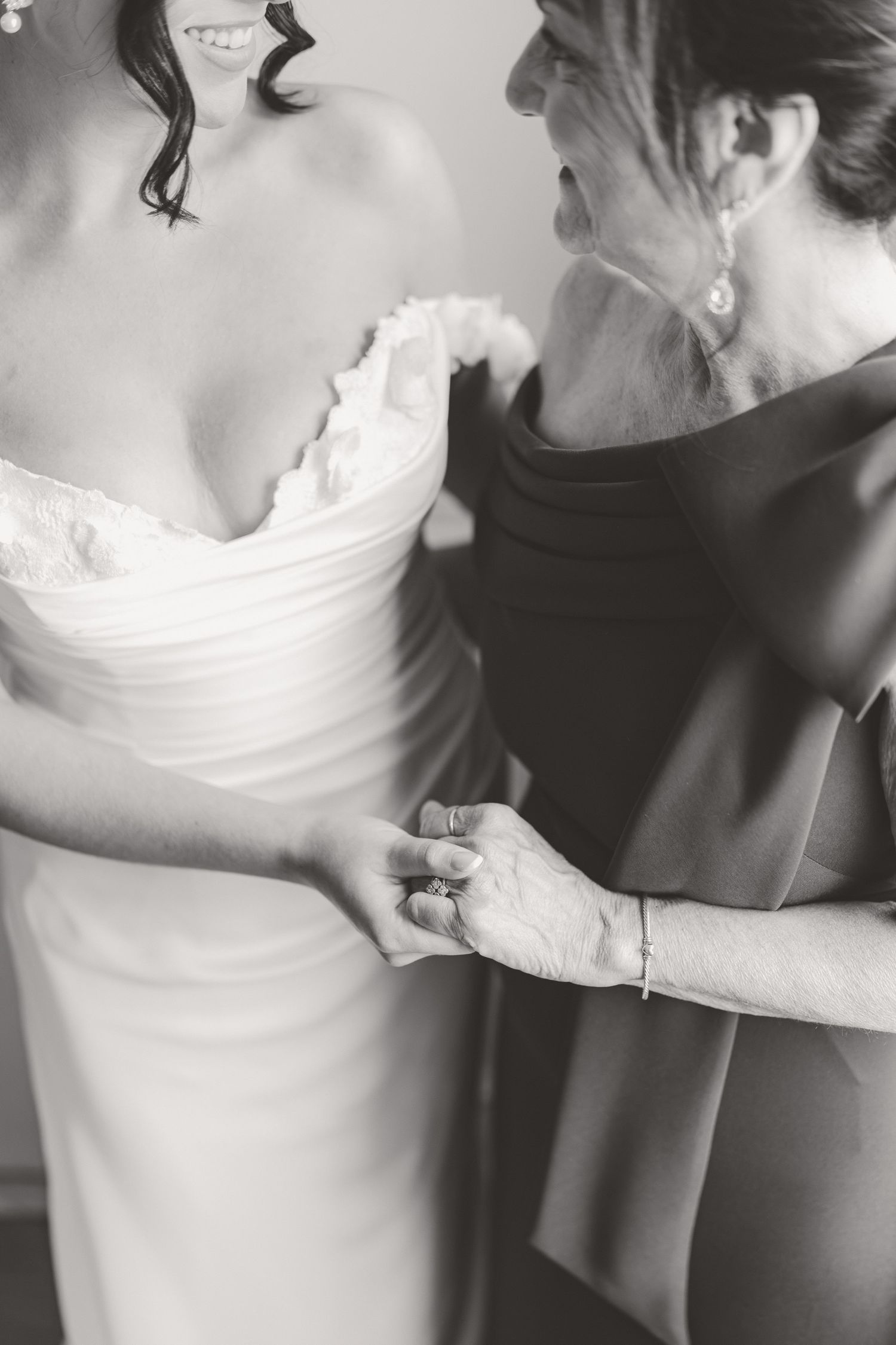 Black and white photo of mother helping bride with her wedding gown before ceremony.