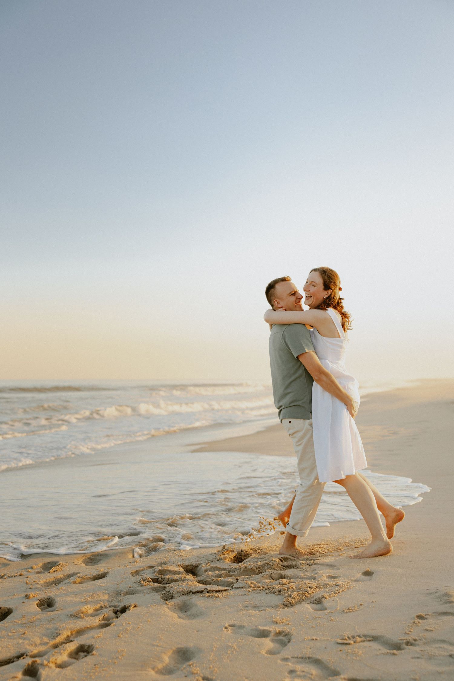 Happy couple embraces on sandy beach at golden sunset with ocean waves in background.